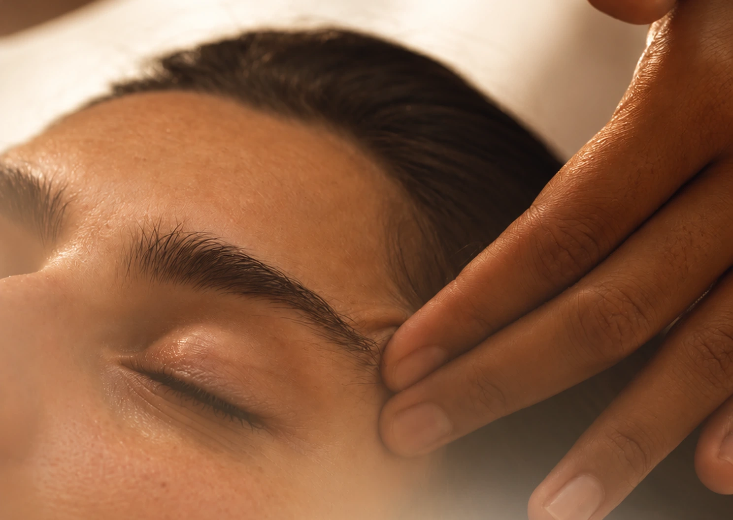 Massage crânio-facial : pression douce des doigts sur la tempe d'une femme détendue, yeux fermés, lors d'un soin à Biarritz