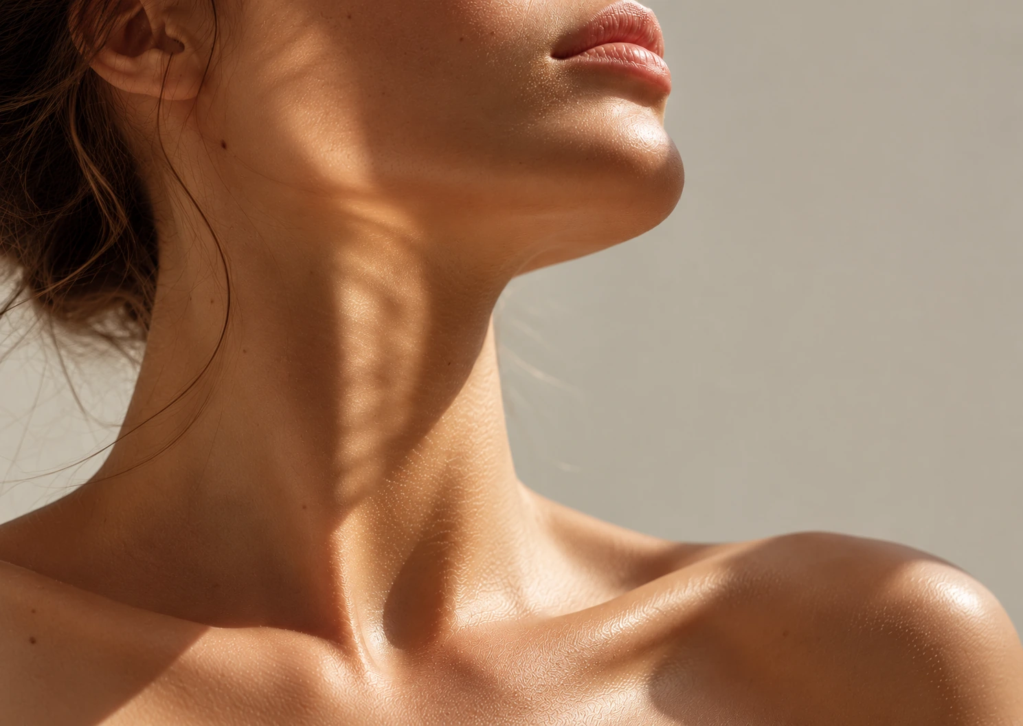 Nuque, cou et décolleté d'une femme, tête légèrement relevée, peau lumineuse éclairée par le soleil, illustrant un massage cervical à Biarritz